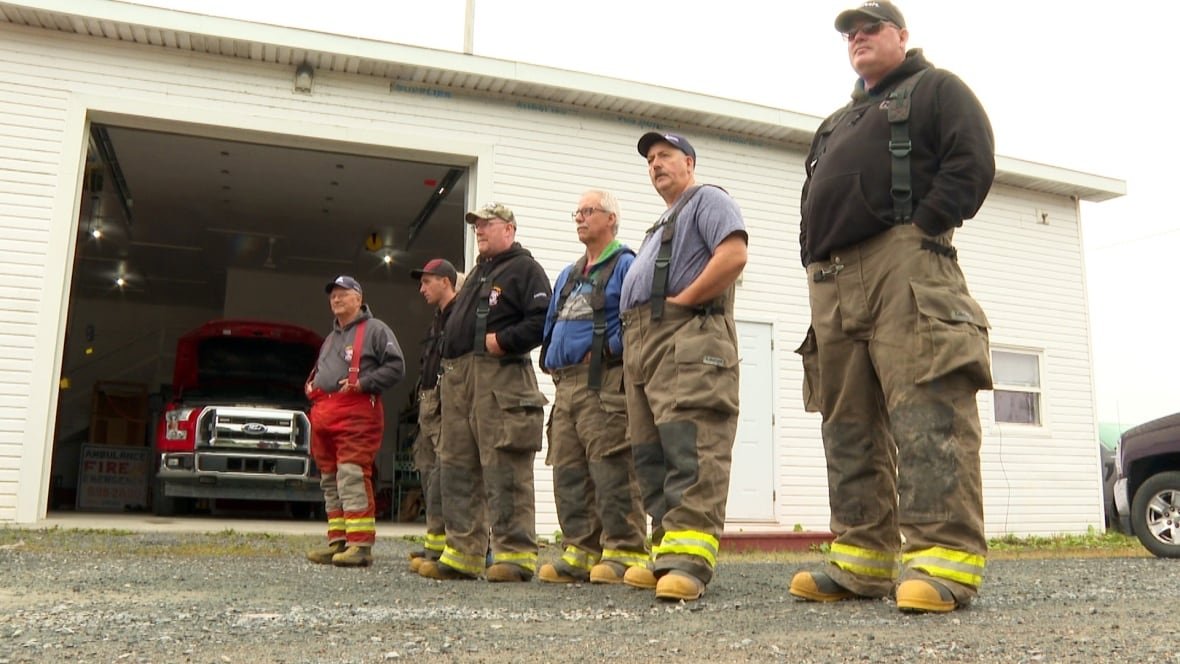 north-shore-volunteer-fire-department-1 Six men standing in line outside garage with door open and red truck inside.
