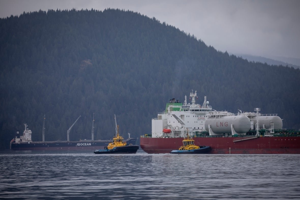 pipeline-trans-mountain-oil-tankers An oil tanker is seen next to two smaller tug boats on a water body, with mountains in the background.