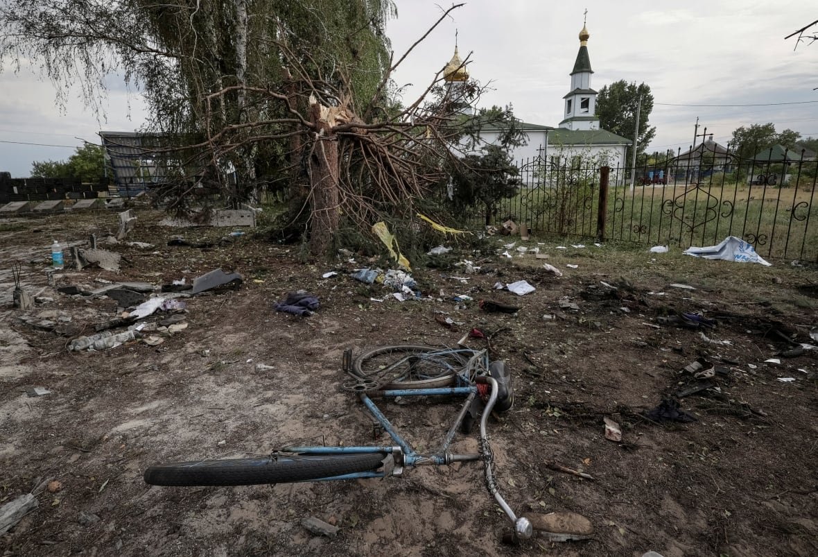 ukraine-crisis-attack-yarova A heavily damaged tree and a bicycle on dirt ground are shown in the foreground of the photo, with a building that resembles a church in the background.