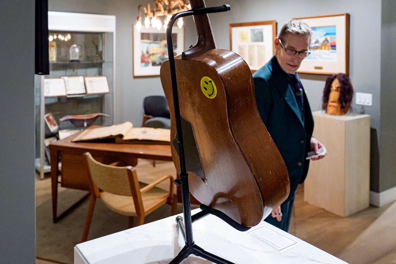 A person looks at a guitar on display at a showroom of an auction house where there are framed paintings and glass displays in the background.