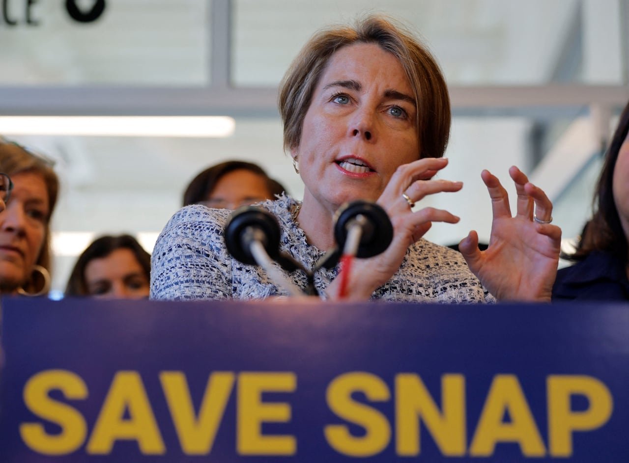 A woman with ear-length hair gestures at a podium with a sign reading "Save Snap."