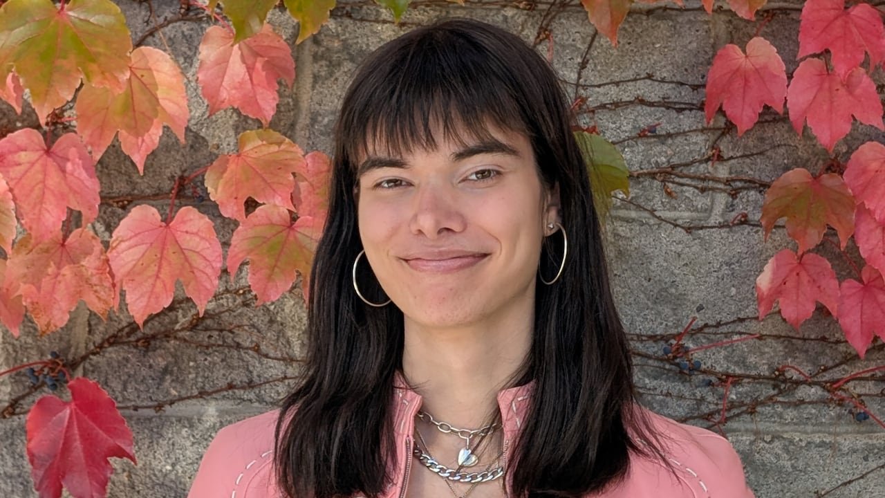 A woman with shoulder-length brown hair and a pink jacket smiling at the camera.