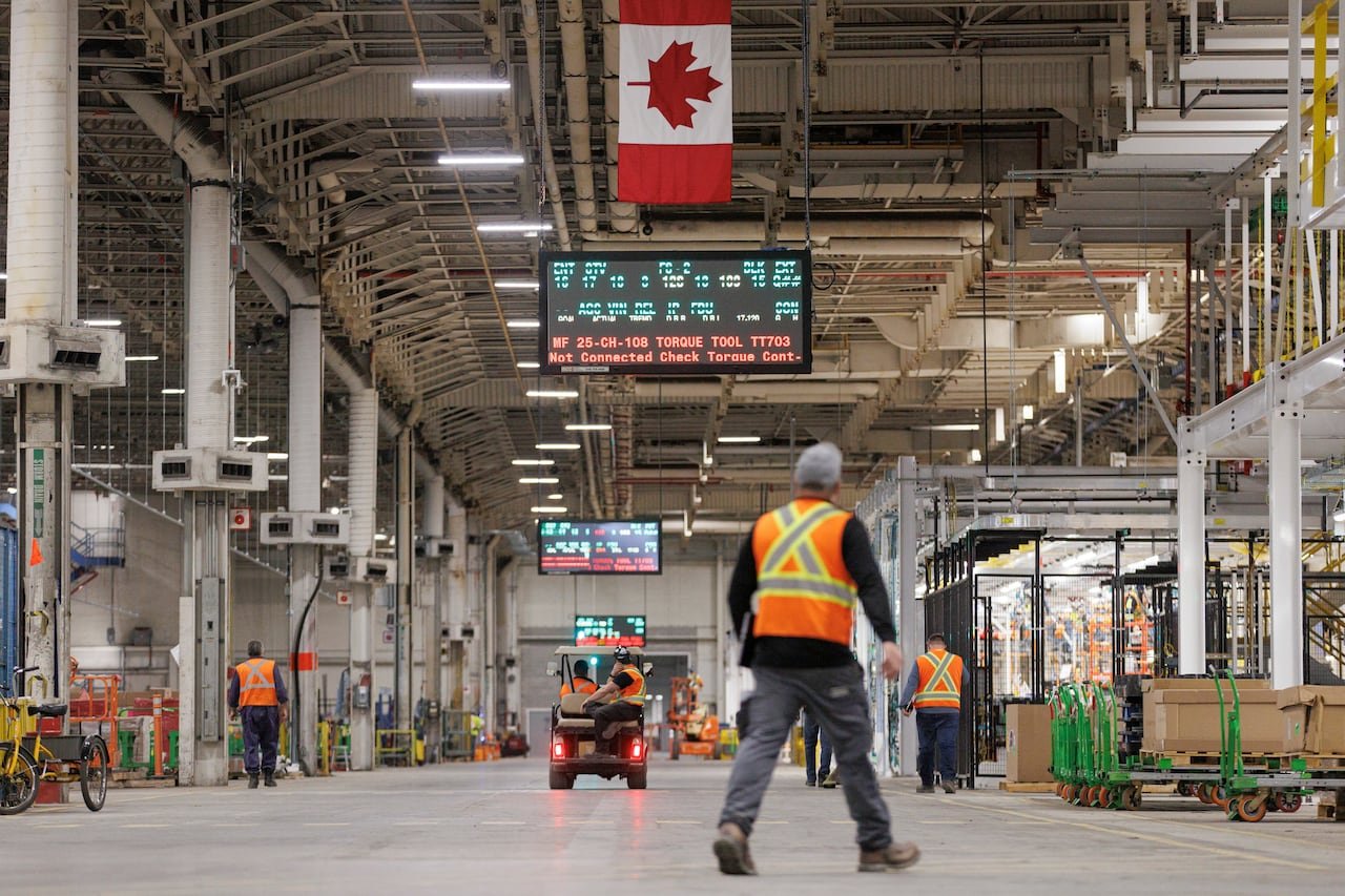 default-11 workers in orange reflective vests walk on the floor of a production plant where cars are being assembled