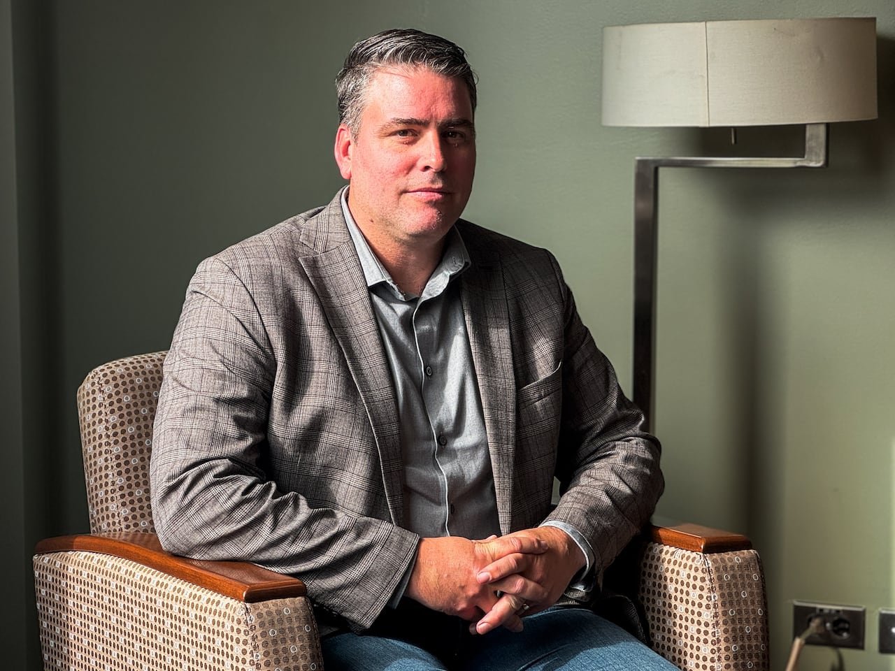 A man sits on a chair in a casual suit.