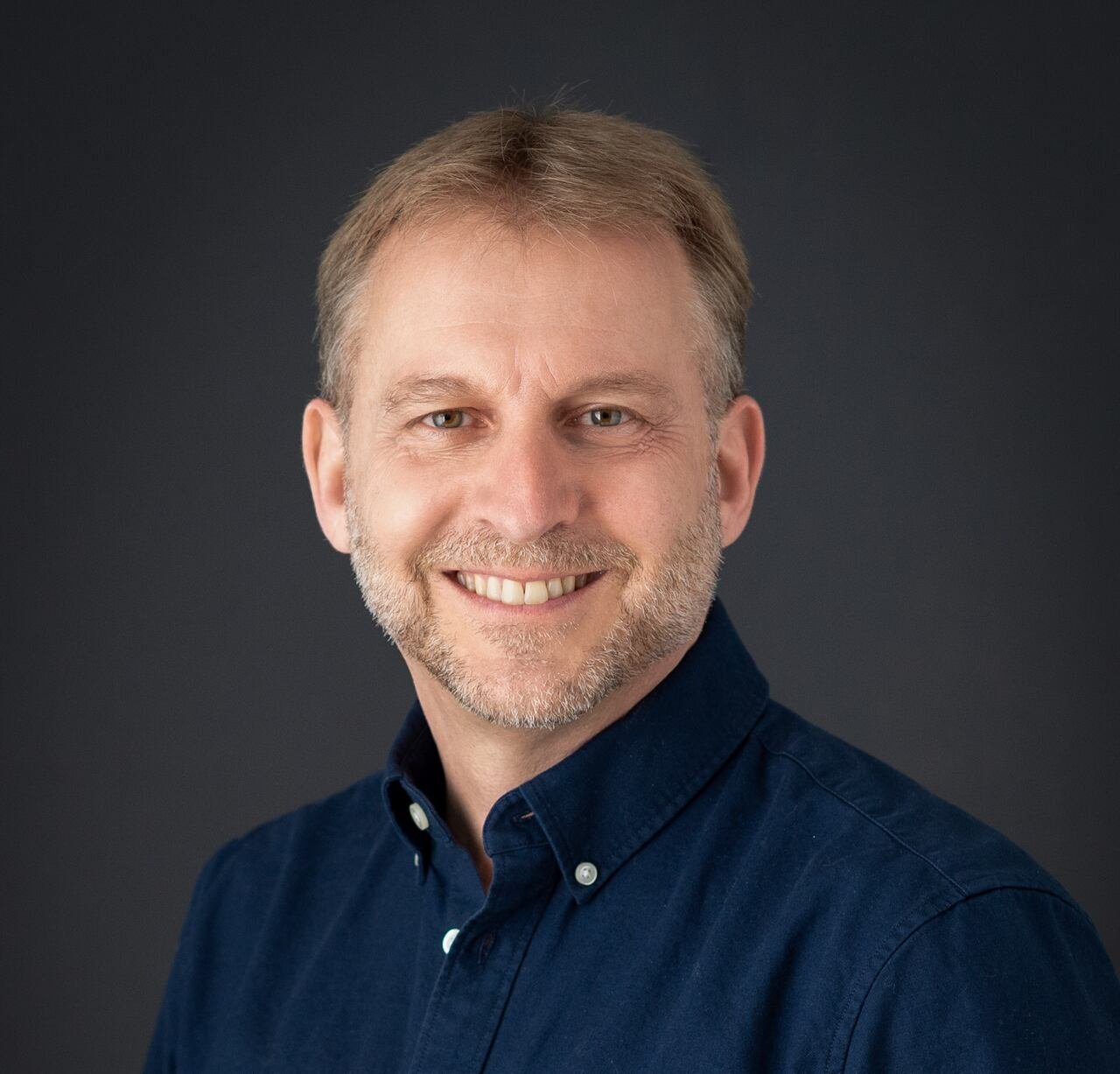 Man smiling in blue shirt against dark background