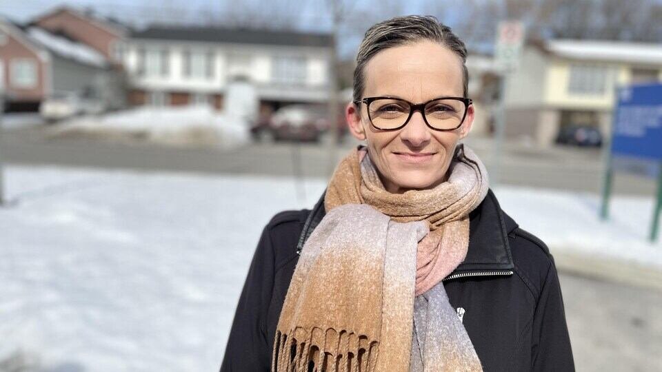 A woman stands outside with a scarf and snow around her.